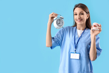 Female dentist with alarm clock and jaw model on blue background