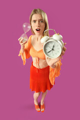 Shocked young woman with alarm clock and hourglass on purple background