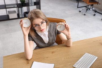 Tired young businesswoman with alarm clocks at table in office. Time management concept