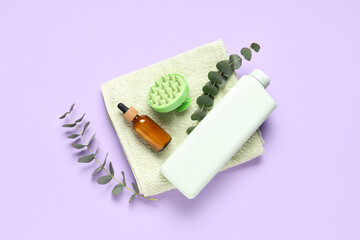 Hair scalp massager with bottle of shampoo, cosmetic oil and towel on lilac background