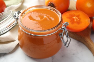 Delicious persimmon jam and fresh fruits on white marble table, closeup