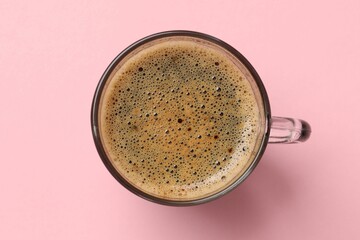 Aromatic coffee in glass cup on pink background, top view