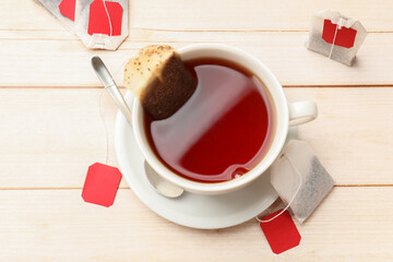 Tea bags, cup of hot beverage and spoon on light wooden table, flat lay