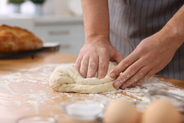 Making bread. Man kneading dough at wooden table in kitchen, closeup