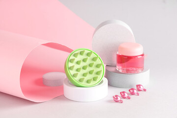 Decorative podiums with hair scalp massager, jar of cosmetic cream and capsules on colorful background