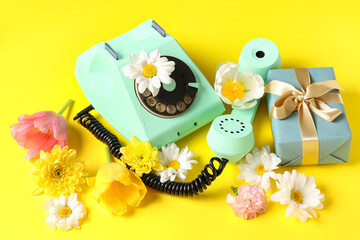 Retro telephone with gift box and beautiful flowers on yellow background. International Women's Day