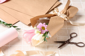 Composition with mini bouquet of beautiful spring flowers in wrapping paper, ribbon and scissors on beige tile background. International Women's Day