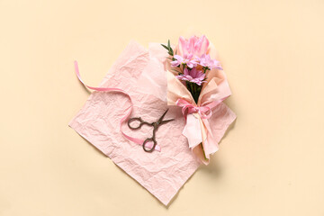 Mini bouquet of beautiful spring flowers in wrapping paper with ribbon and scissors on beige background. International Women's Day