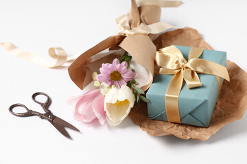 Fototapeta na wymiar Mini bouquet of beautiful spring flowers in wrapping paper with scissors and gift box on white background. International Women's Day