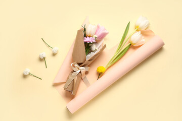 Composition with mini bouquet of beautiful spring flowers in wrapping paper on yellow background. International Women's Day