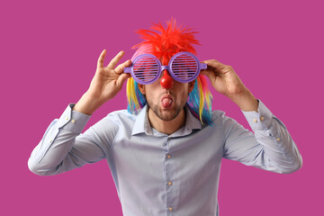 Young businessman in funny disguise showing tongue on purple background. April Fools' Day celebration