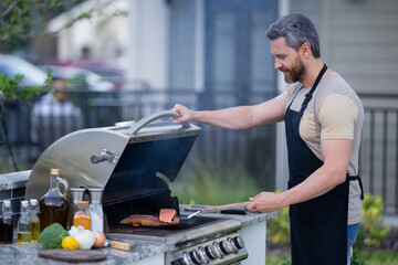 Men cooking on barbecue grill in yard. Cook at a barbecue grill preparing meat. Guy cooking meat on barbecue for summer family dinner at the backyard of the house.