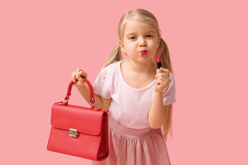 Cute little girl with stylish red handbag and lipstick on pink background