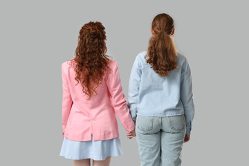 Stylish redhead sisters on grey background, back view