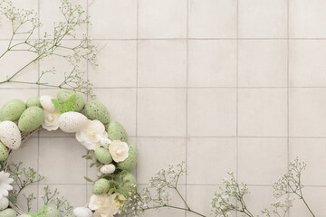 Easter wreath made of flowers, eggs and butterflies with sprigs of gypsophila on white tile table
