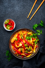 Stir fry turkey breast with red paprika and zucchini with sesame seeds, garlic, ginger and soy sauce in frying pan. Black table background, top view