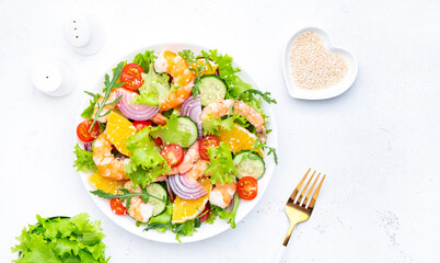 Fresh delicious shrimp salad with orange, lettuce, tomatoes, cucumbers, onions and sesame seeds with olive oil, white background, top view