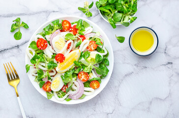 Fresh salad with squid, eggs, cherry tomatoes, onion, lamb lettuce and olive oil with lemon juice dressing, marble table background, top view