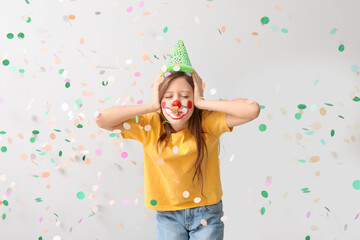 Fototapeta premium Funny girl with clown makeup, party hat, whistle and confetti covering ears on white background. April Fool's Day celebration