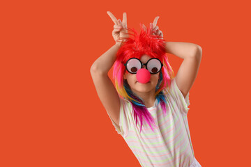Funny girl in clown costume and party glasses on orange background. April Fool's Day celebration - obrazy, fototapety, plakaty