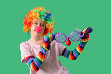 Funny girl in clown costume with party glasses on green background. April Fool's Day celebration