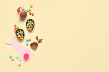 Chocolate Easter eggs with candies and paper bunny on yellow background