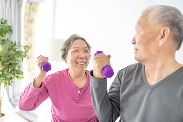 Happy Asian senior couple doing exercises with dumbbells indoors.