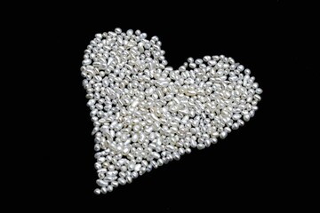 Saint Valentine day themed photo of little white Keshi freshwater pearls on black background in the heart shape. Holiday card made of precious organic gems used in jewelry.