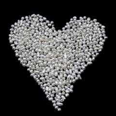 Saint Valentine day themed photo of little white Keshi freshwater pearls on black background in the heart shape. Holiday card made of precious organic gems used in jewelry.