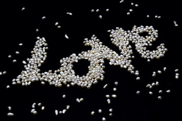 Valentine day themed photo of beautiful small freshwater pearls, white Keshi organic gems for use in jewelry. Letters L O V E drawn in little clear dots on black background.