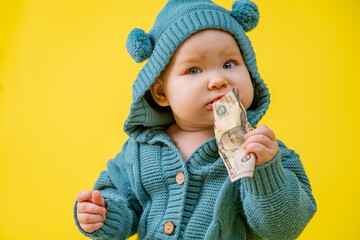 Cute kid chewing dollars on a yellow background. Baby in a blue knitted suit with money on a yellow background.