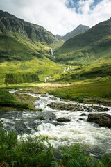 Vertical shot of a river surrounded by the mountains and meadows in Scotland