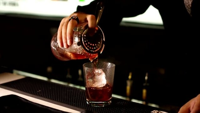 bartender pouring negroni cocktail into glass with ice at bar counter footage
