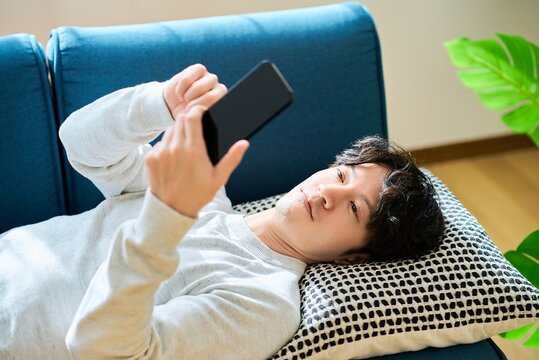 スマートフォンを持ってソファーベッドで横になる若い男性