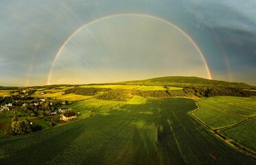 an aerial shot of a large field with a rainbow in the sky