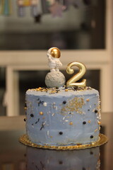 a close up of a blue cake with gold sprinkles with number 2 candle and a spaceman on the moon cake...