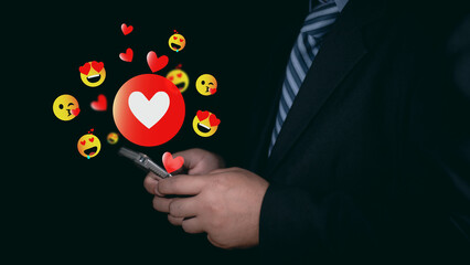 A businessman uses a mobile phone to send a heart emoji to his girlfriend on Valentine's Day. Valentine's Day concept,  love care, Man wearing a suit holds a mobile phone forwarded heart emoji.