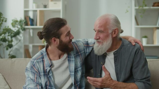 Young and elderly men share life experiences, sitting on a couch, discussing personal stories, psychological support, cross-generational understanding, heart-to-heart talks, family communication