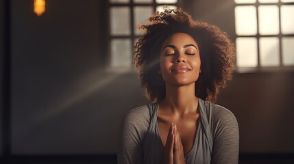 Mature woman meditating with her eyes closed and her hands in prayer position. Black woman with dreadlocks practicing yoga in a studio. Happy middle-aged woman maintaining a healthy lifestyle - obrazy, fototapety, plakaty