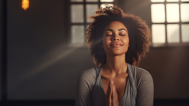 Mature woman meditating with her eyes closed and her hands in prayer position. Black woman with dreadlocks practicing yoga in a studio. Happy middle-aged woman maintaining a healthy lifestyle