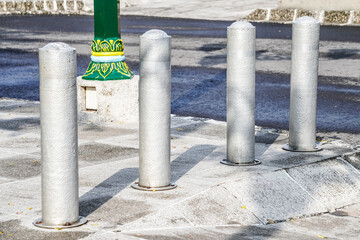 Metallic long inground bollard pole barrier between asphalt road and sidewalk to protect...