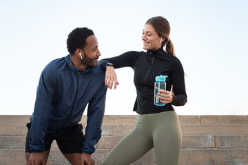 Happy multiracial couple taking a break after running and working out together outdoors.Female holding water bottle