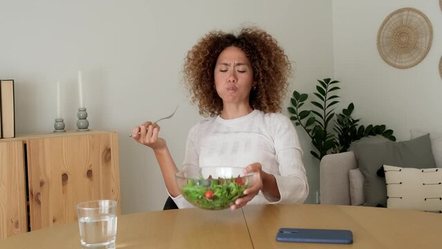 Young multiracial woman eating healthy salad while using phone at home. 4k resolution video.