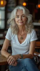 Old Caucasian woman in white t-shirt and jeans sitting at table at modern cafe.