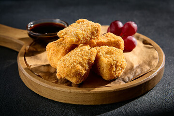 Fried cheese with grapes and berry jam on a wooden serving board, a delightful blend of textures and flavors