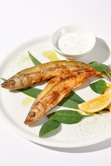 Grilled vendace fish with lemon and sour cream on a white plate, ideal for culinary presentations and food marketing