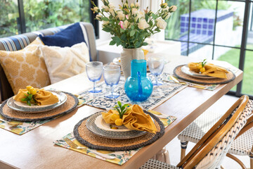 Plate setting with yellow handkerchief on wood table with artificial flowers on the dining table.