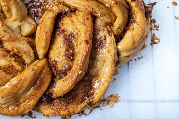 Roscón de reyes Kringle Estonia. Braided sponge cake with cinnamon, butter, walnuts or almonds and icing sugar on a rack and white baking paper.