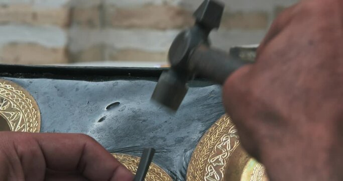 A master embosser creates a pattern on a copper plate using ancient technologies.