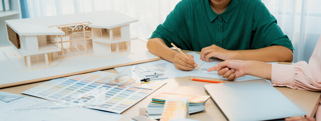Professional architect drafts blueprint from project manager advice on table with house model,...